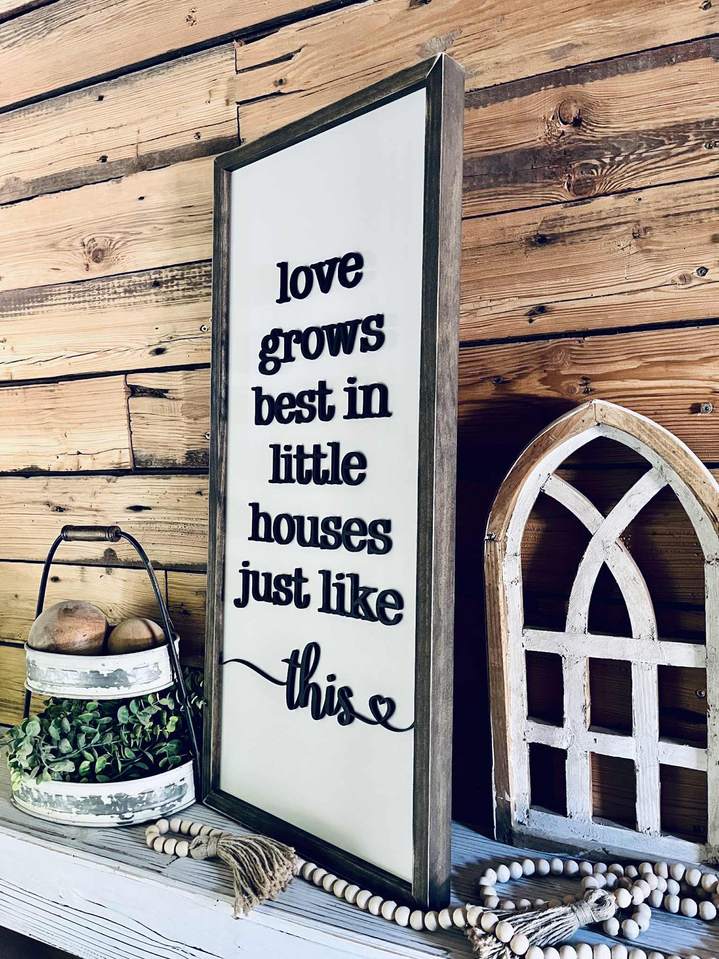 Decorative sign with text 'love grows best in little houses just like this' on a wooden wall.