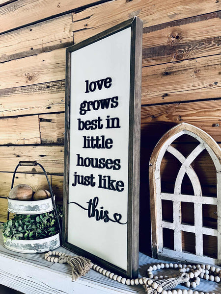 Decorative sign with text 'love grows best in little houses just like this' on a wooden wall.