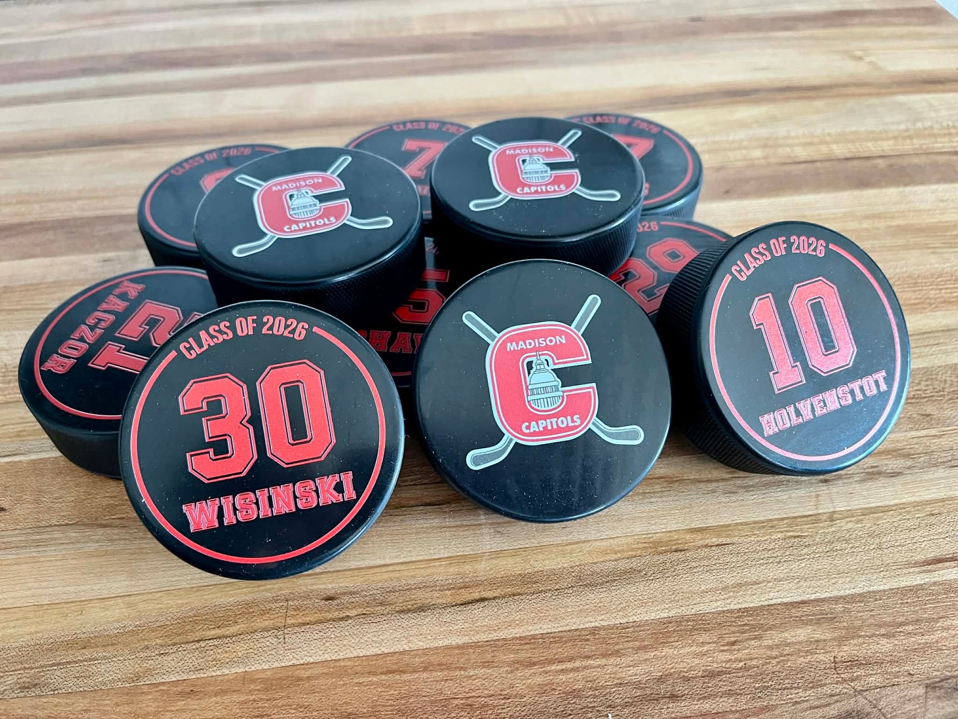 Custom double-sided hockey pucks with team logo on front and player name and number on back for senior gifts.