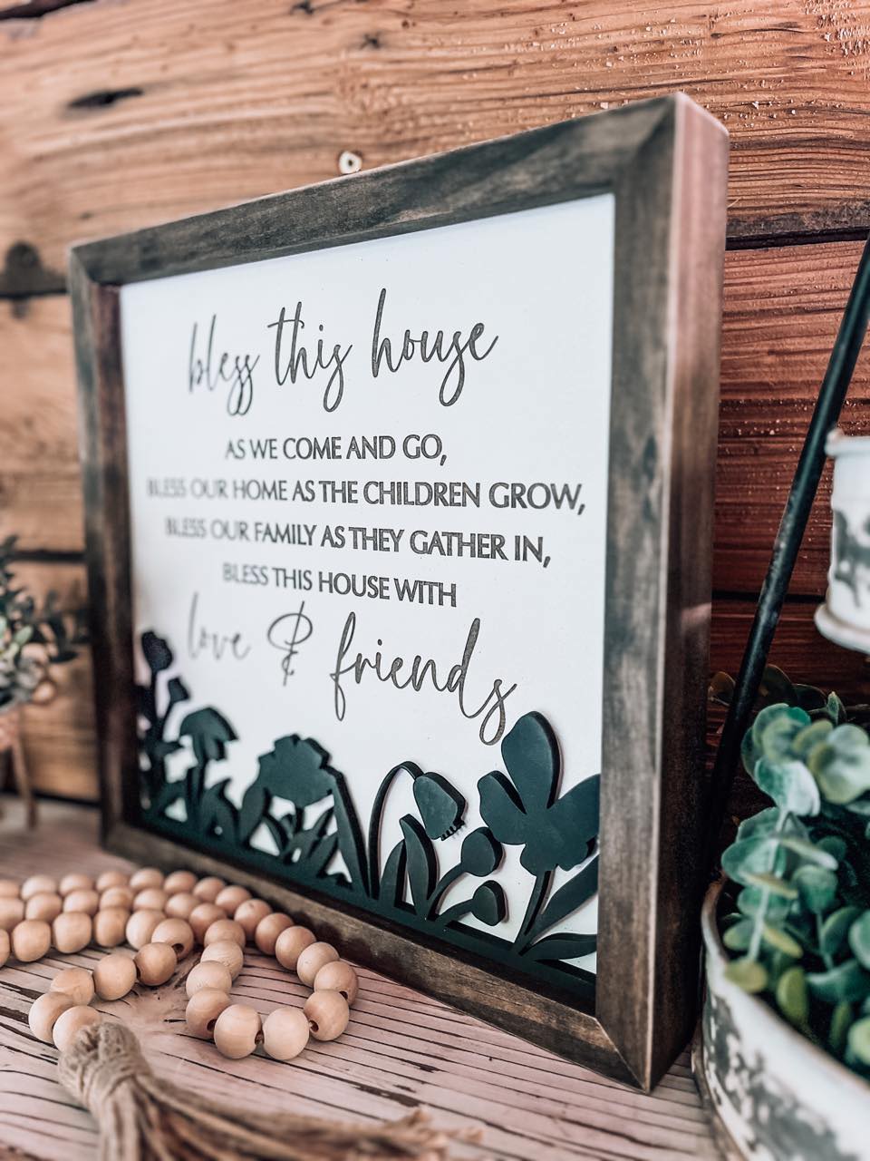 Close-up of 3D laser-cut black floral detail and engraved lettering on a white rustic wood background.
