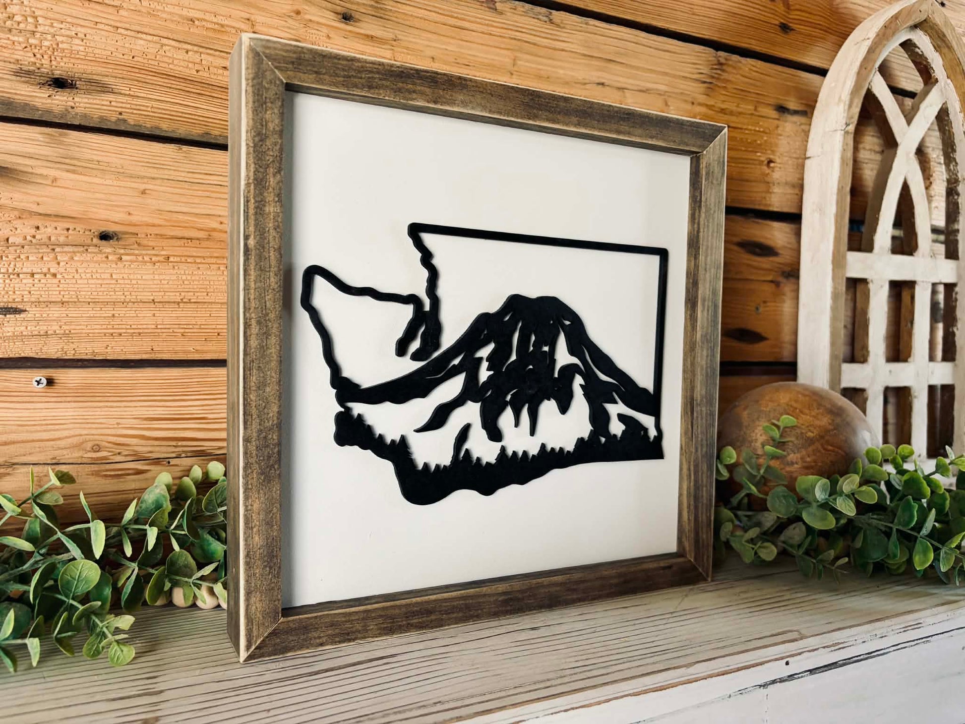 Framed black and white mountain silhouette on a wooden shelf with decorative elements.