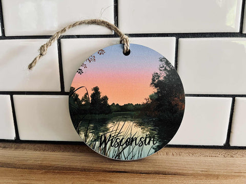 Round MDF ornament with UV-printed Wisconsin sunset and black ‘Wisconsin’ text, jute hanger attached