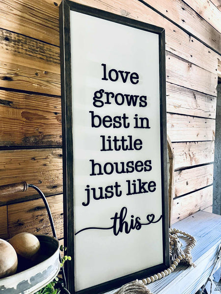 Framed sign with 'love grows best in little houses just like this' text on a wooden wall.