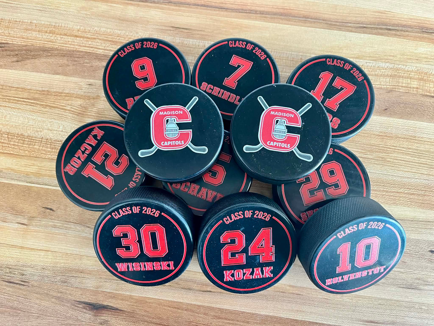 Personalized hockey pucks featuring individual player names and numbers in a high-quality UV print.