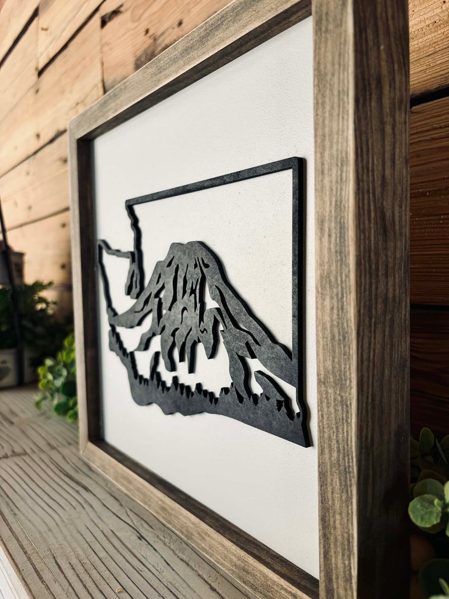 Framed artwork of a mountain silhouette on a wooden wall.
