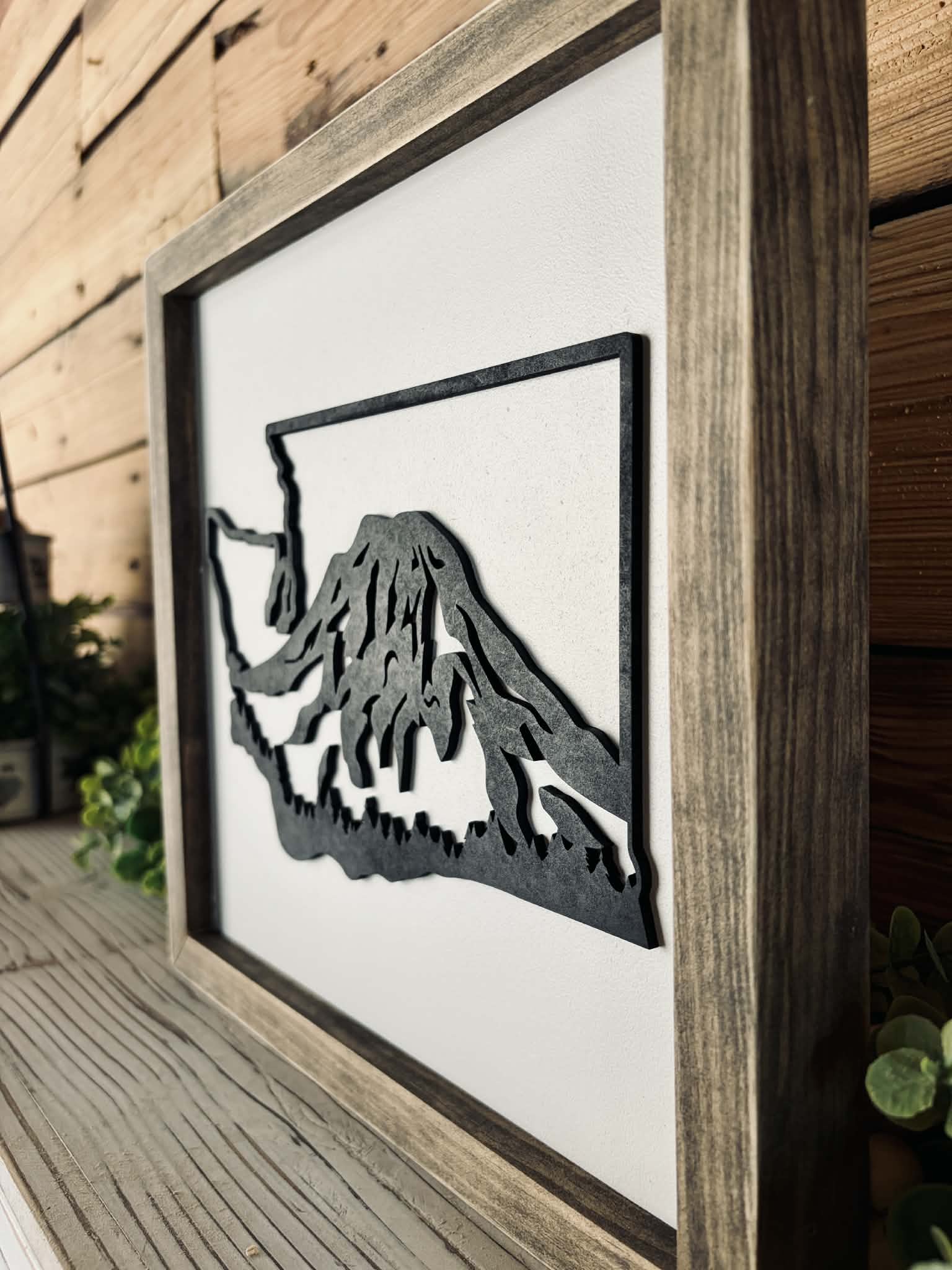 Framed artwork of a mountain silhouette on a wooden wall.