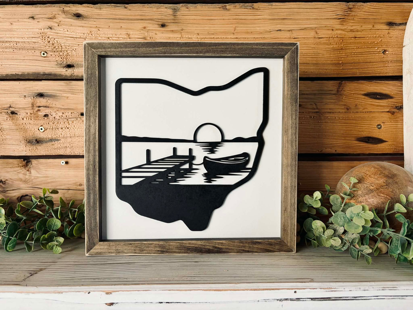 Handcrafted 12x12 framed wood sign featuring a 3D layered silhouette of Ohio with a laser-cut lake scene including a boat, dock, and sunset.